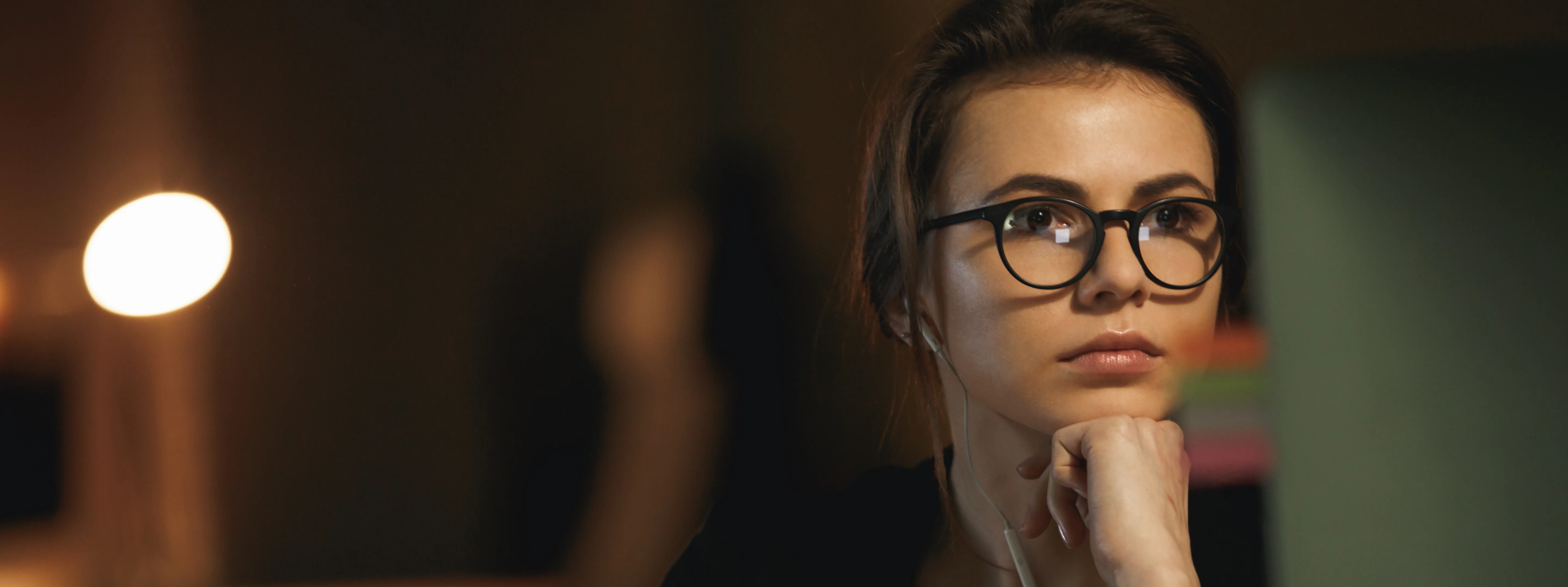 A woman with glasses looking at her screen at night